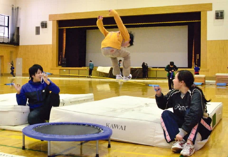写真:小型のトランポリンを使った運動をする児童とそれを指導する2人の学生