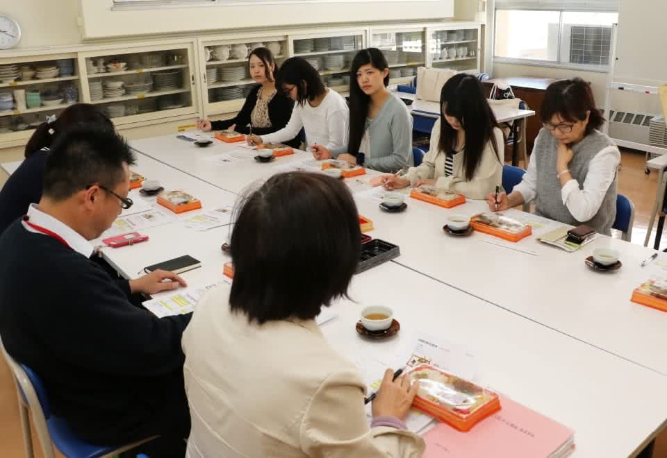 写真:マルイとの弁当開発会議で試作品を試食しながら議論する人見研究室の学生たち・人見准教授とマルイ社員