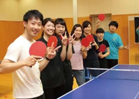 写真：卓球台の前でラケットを持つ笑顔の卓球サークルのメンバーたち