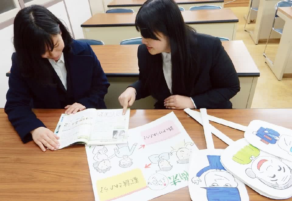 写真:女性が2人で机の上に手作りの教材を置いて体験学習をしている様子