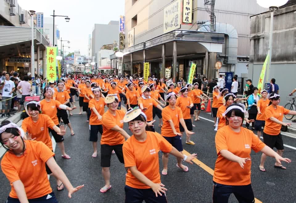 写真:オレンジ色のTシャツを着て、頭にミマッパちゃんのお面を付け、顔にメイクをして一生懸命ごんごおどりを踊る幼児教育学科の学生たち