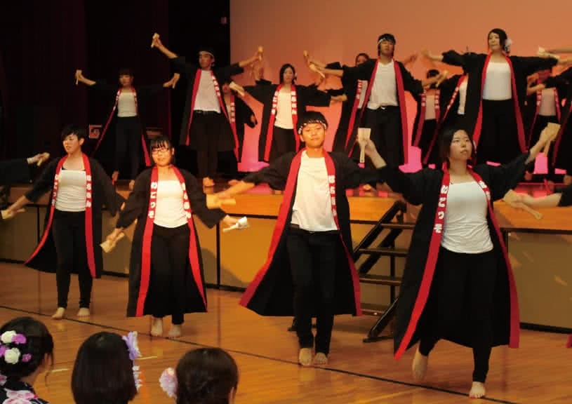 写真:屋内のステージで揃いの黒い衣装を着てよさこいを踊る高知県人会のメンバーたち