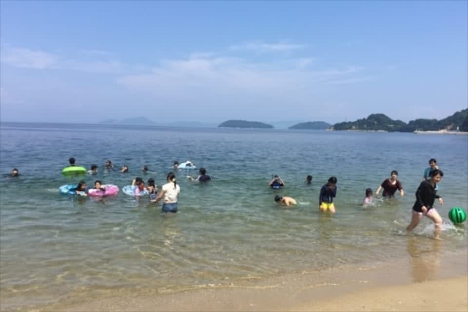 写真:海で、ボールを使って遊んだり、浮き輪を使って泳いだりする学生と笠岡諸島の子どもたち