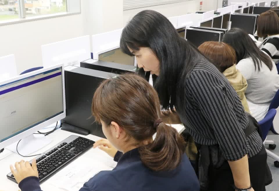 写真:パソコンを操作する学生にサポートスタッフが使い方を指導している