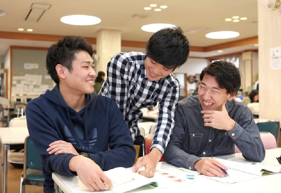 写真:学生ホールで友だち二人と教科書やノートを広げて試験対策をするBさん