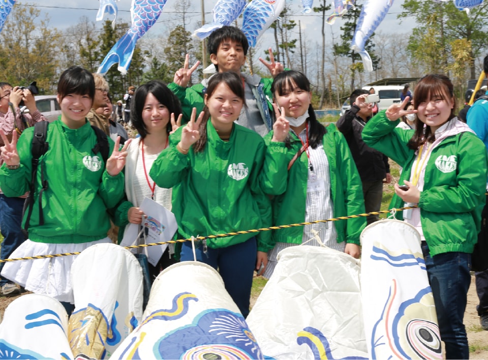 写真：揃いの緑色のジャケットを着て鯉のぼりを持つ学生スタッフたち