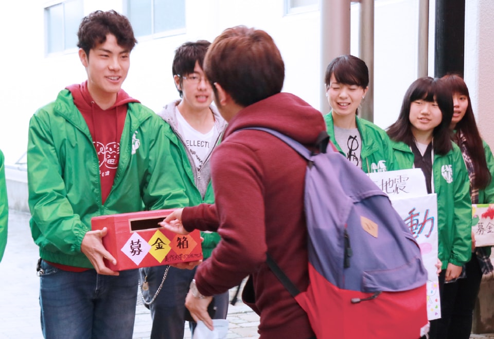 写真：揃いの緑色のジャケットを着て募金活動を行う学生スタッフたち。
