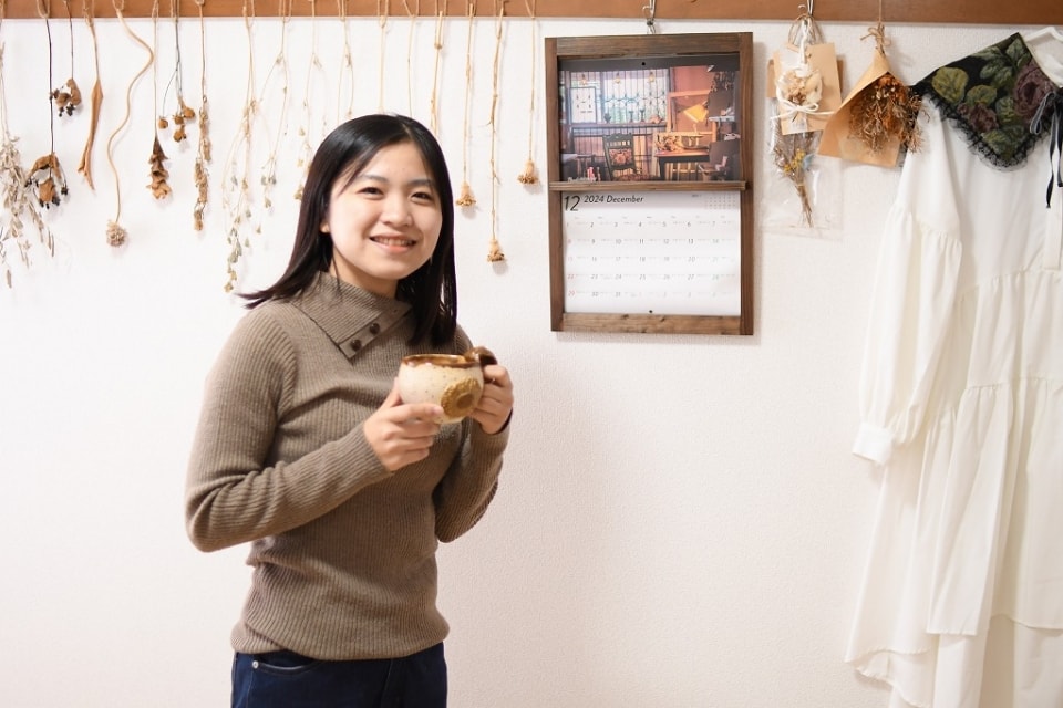 写真:マグカップを手にして、笑顔を向けるMさん