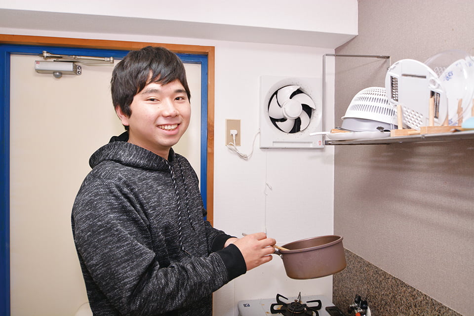 写真:片手鍋を持って料理するOさん