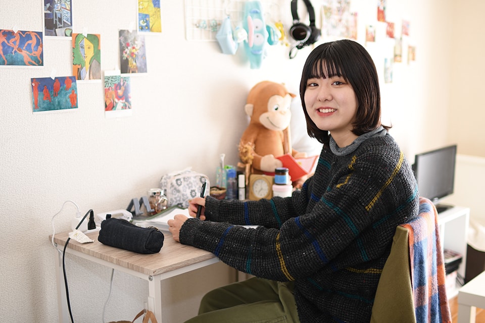 写真:机で勉強しながら、こちらに体を向けて笑顔を見せるKさん