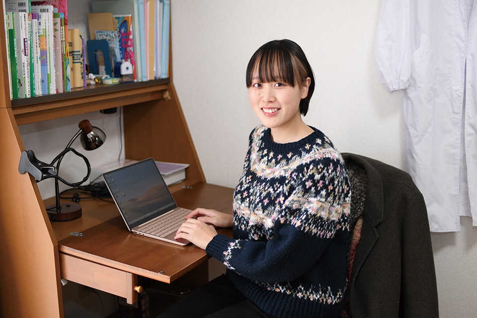写真:机の上にあるノートパソコンを使いながら、笑顔を向けるYさん