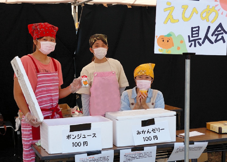 写真：エプロンと三角巾、マスクを付け、白梅祭でポンジュースとみかんゼリーを100円で販売する愛媛県人会の3人のメンバー