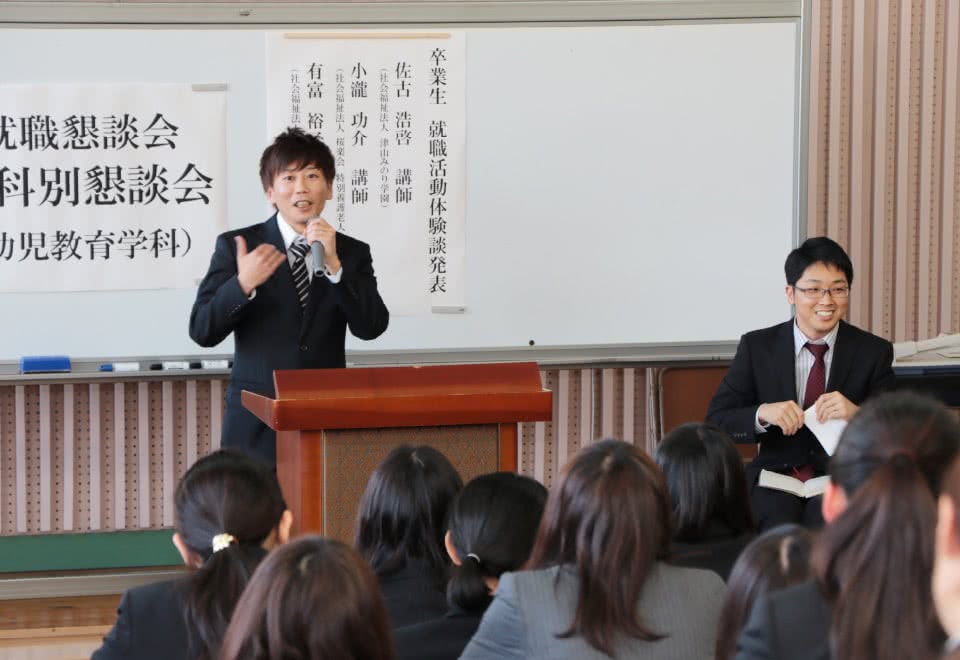 写真:卒業生の講話会の壇上で語る男子卒業生と、それを聞く学生たち