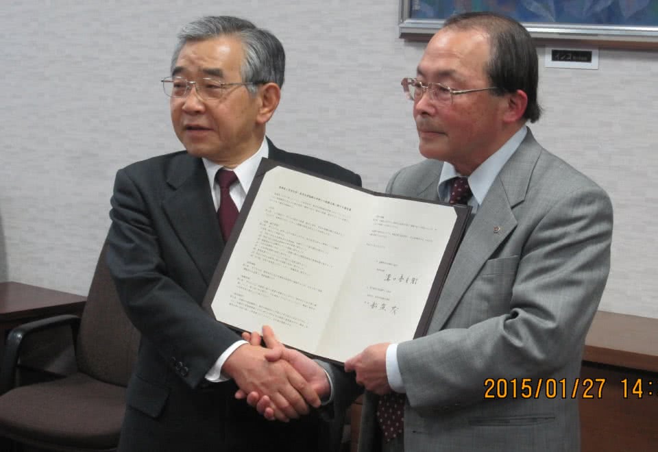 写真：島根県との締結式で協定書を手に持ち、握手している溝口善兵衛知事と船盛茂学長