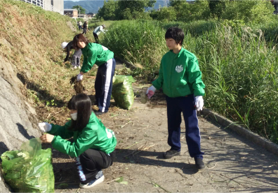 写真：揃いの緑色のジャケットを着て草抜きのボランティア活動をするボランテティアセンターの学生たち