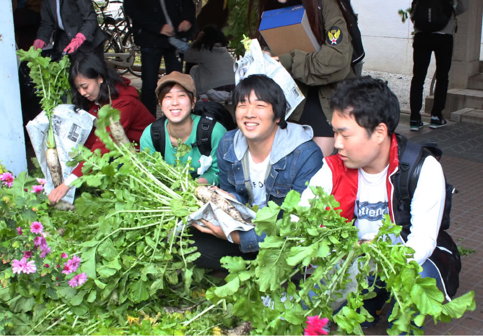 写真：無料野菜市場で並べられた野菜とそれを手に持つ学生たち