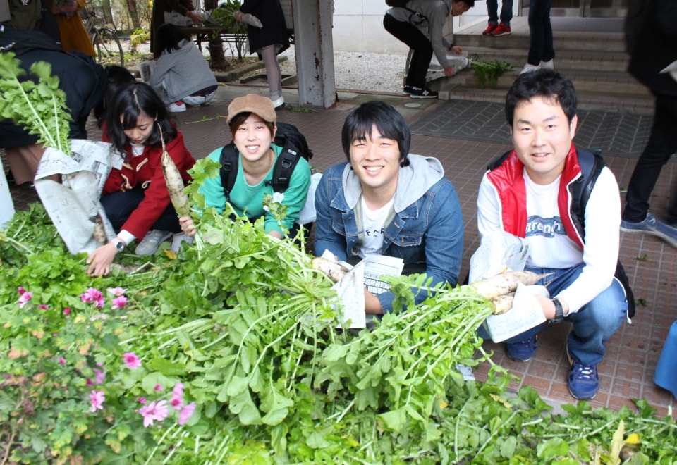 写真：無料野菜市場で並べられた野菜とそれを手に持つ学生たち