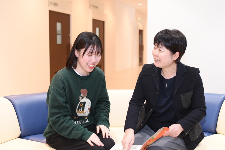 写真:明るい廊下のソファで、学生と職員が資料を手に楽しそうに会話している様子