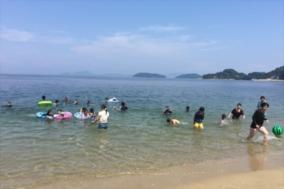 写真：海で、ボールを使って遊んだり、浮き輪を使って泳いだりする学生と笠岡諸島の子どもたち