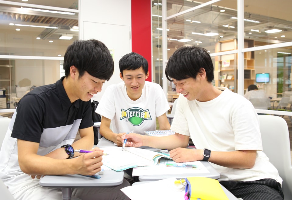広げたノートを囲んで会話する3人の男子学生