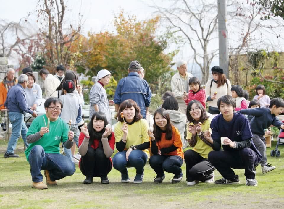 写真：公園で手に食べ物をもってしゃがんで写真に収まる学生たち