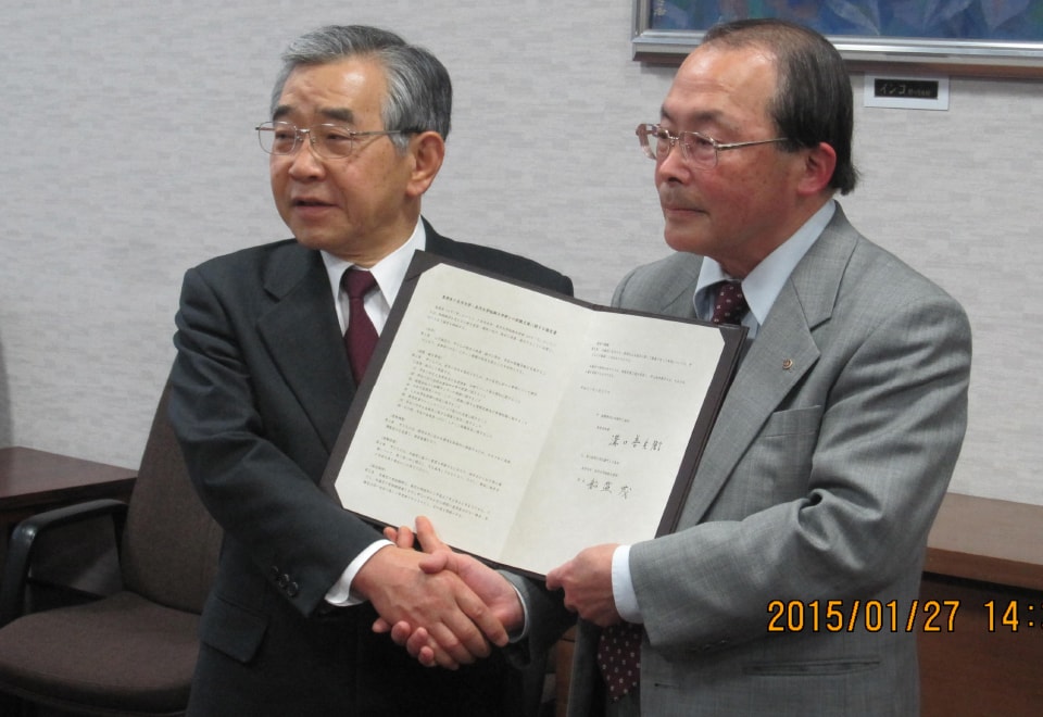 写真:島根県との締結式で協定書を手に持ち、握手している溝口善兵衛知事と船盛茂学長