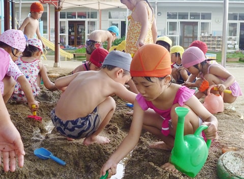 写真：水着を着て砂場で砂遊びをする園児たち