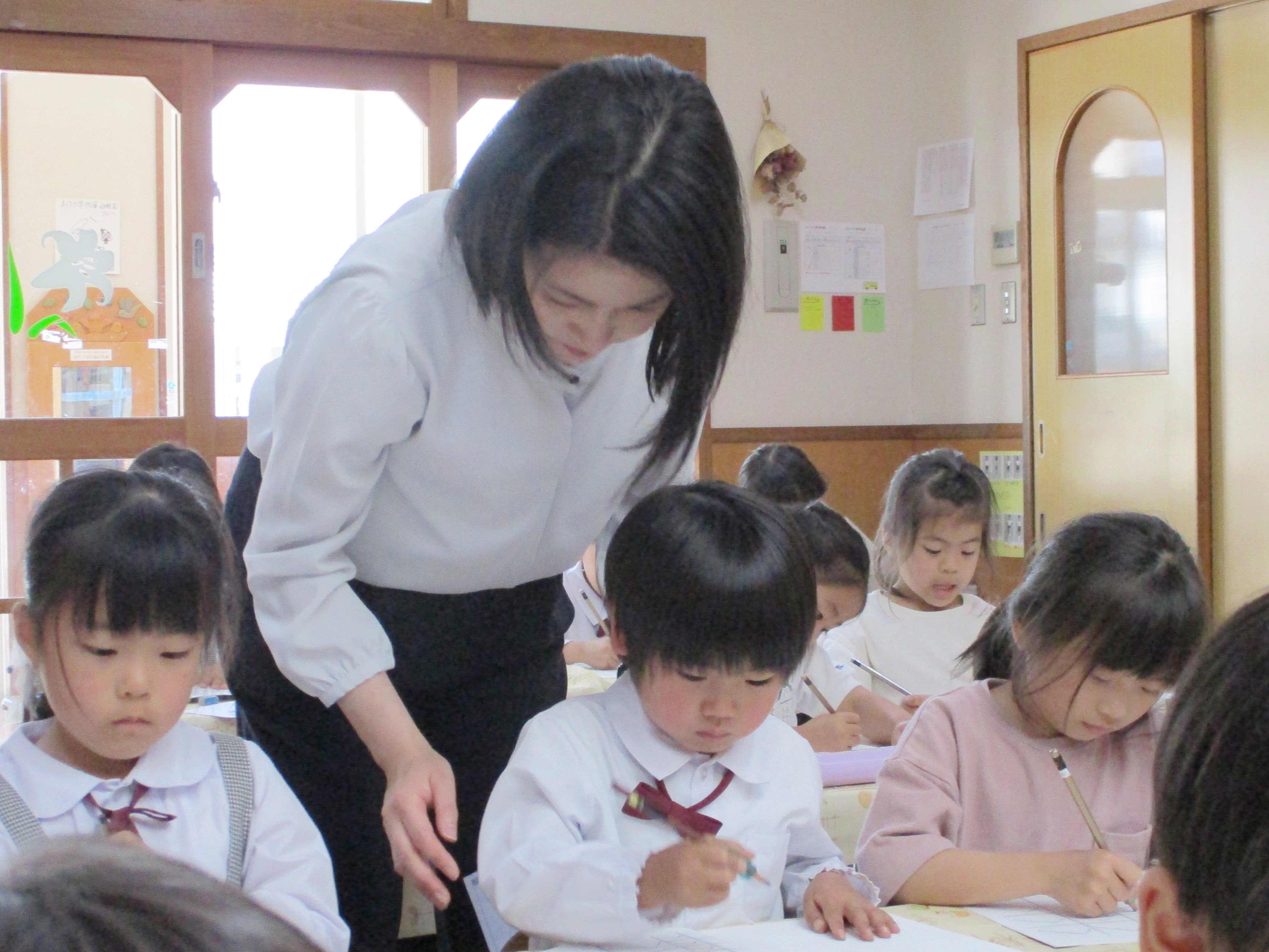 写真：字を書く園児の後ろから指導を行っている西尾先生