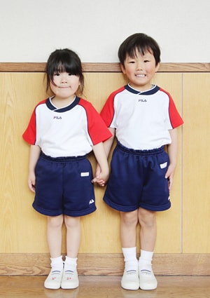 写真：体操服。男女ともに赤い袖と紺色の襟ぐり、白の身ごろのシャツと紺色のショートパンツ