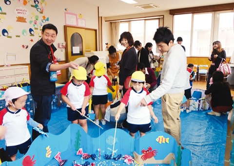 写真：幼稚園まつりで、紙でできた魚を釣る遊びをする園児と保護者たち